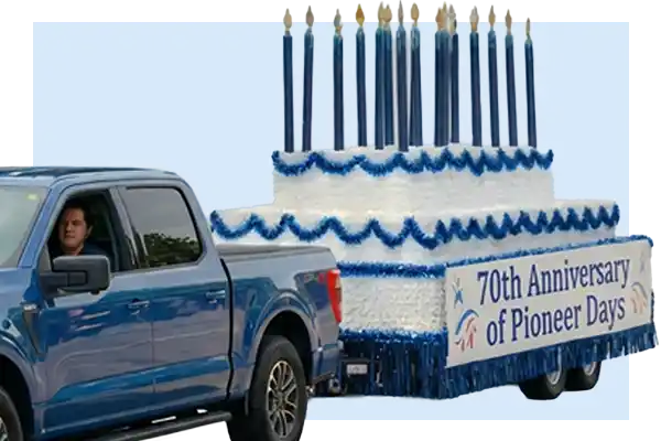 Parade float styled like a tiered white cake with blue trim, tall candles, and a banner reading 70th Anniversary of Pioneer Days.