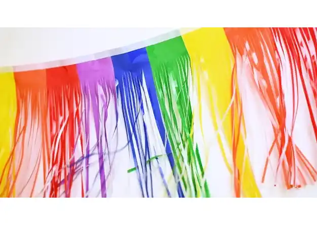 Close-up of rainbow-colored fringe streamers hanging vertically, showing bright multicolor strands for parade decoration.