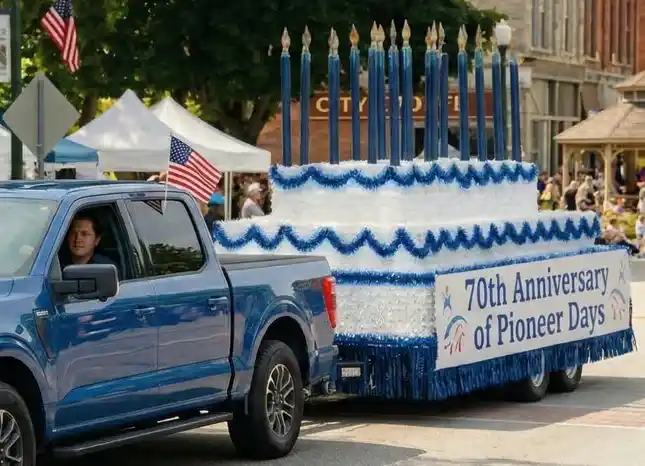 Pickup truck pulling a parade float styled like a tiered cake with blue candles and a 70th Anniversary banner