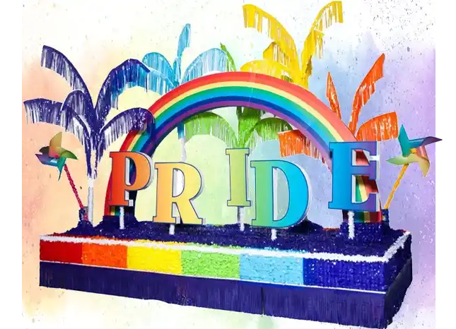 Rainbow Pride parade float featuring large Pride letter sculptures beneath a rainbow arch, with colorful palm-style decorations and a multicolored base.