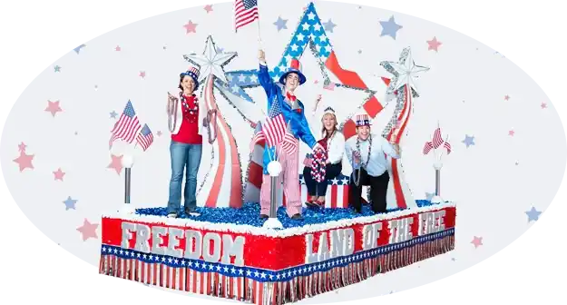 Patriotic parade float featuring large Statue of Liberty sculptures, gold fringe accents, and Land of the Free lettering across the front.