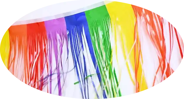 Close-up of rainbow-colored fringe streamers hanging vertically, showing bright multicolor strands for parade decoration.